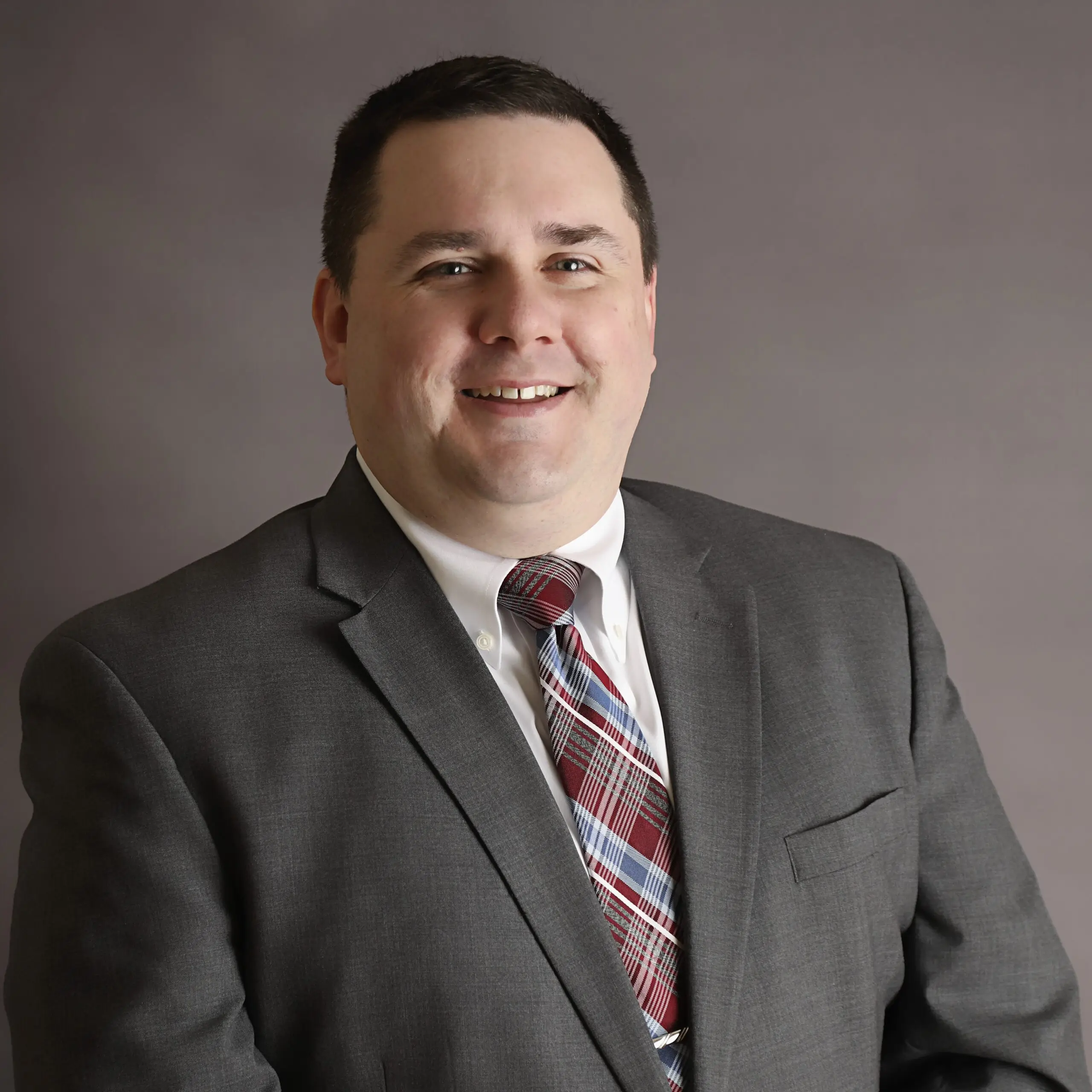 Man in grey suit with red tie smiling.