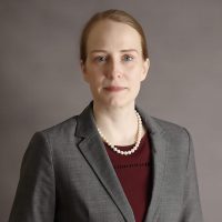 Woman wearing a grey blazer and a pearl necklace.